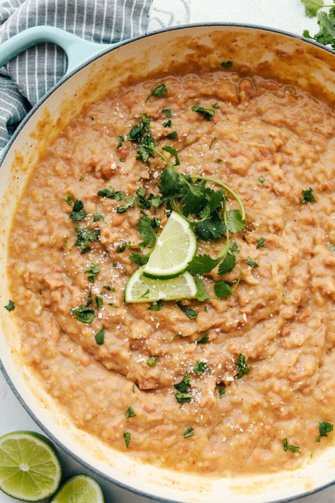 A bowl of refried beans topped with cilantro and limes.