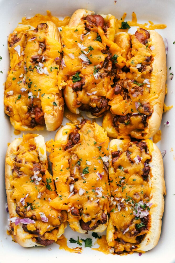 A pan of baked chili dogs covered in cheese and red onions. 