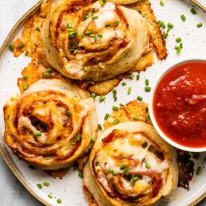 A white plate with pizza pinwheels and a red dipping sauce.