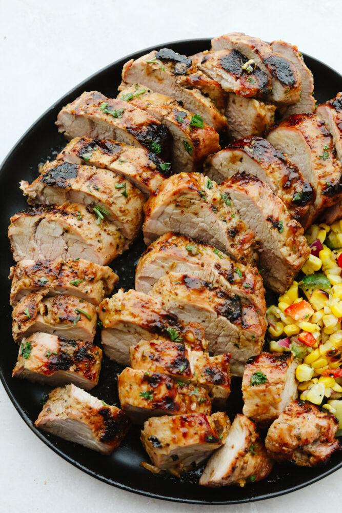 Grilled Honey Dijon Garlic Pork Tenderloin sliced, served with corn.