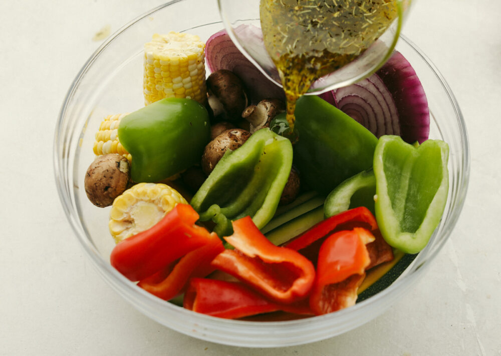 Mixed vegetables in bowl with marinade being poured over it.