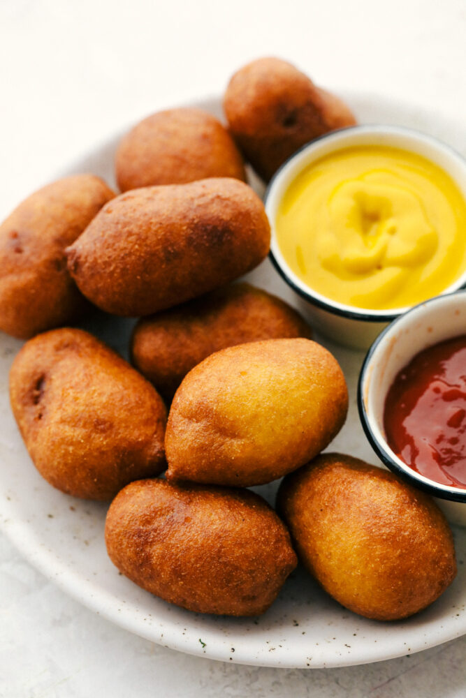 Mini corn dogs on a plate with mustard and ketchup on the side.