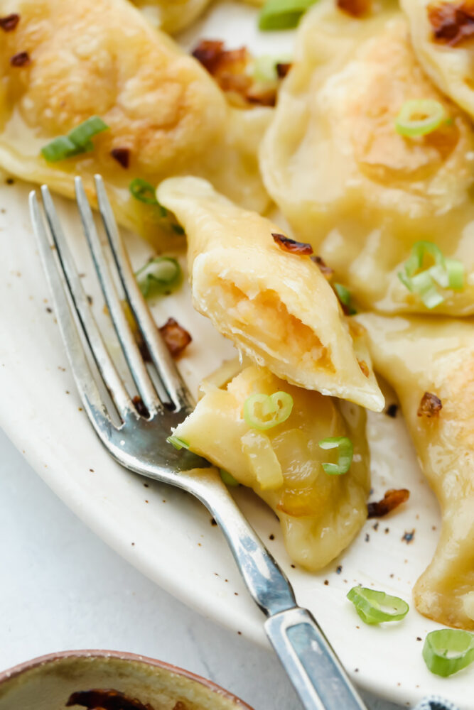 Cutting into a pierogi with a fork showing the potato and cheese filling. 