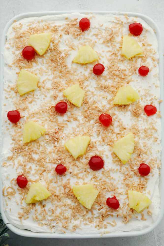 Decorated pina colada poke cake with pineapple, and maraschino cherries. 