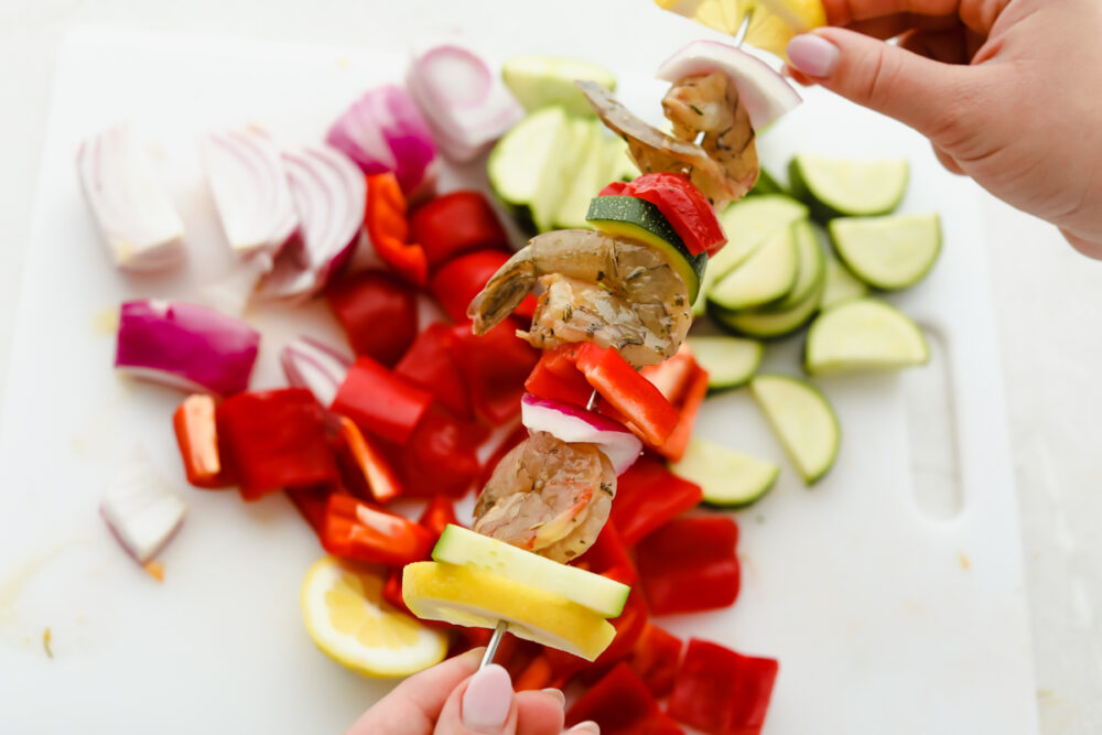 Placing the shrimp and vegetables onto skewers. 