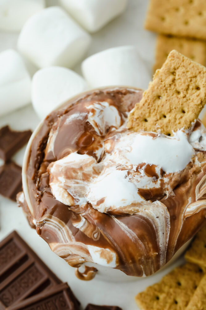 A graham cracker sittin g a pot of s'more dip. 