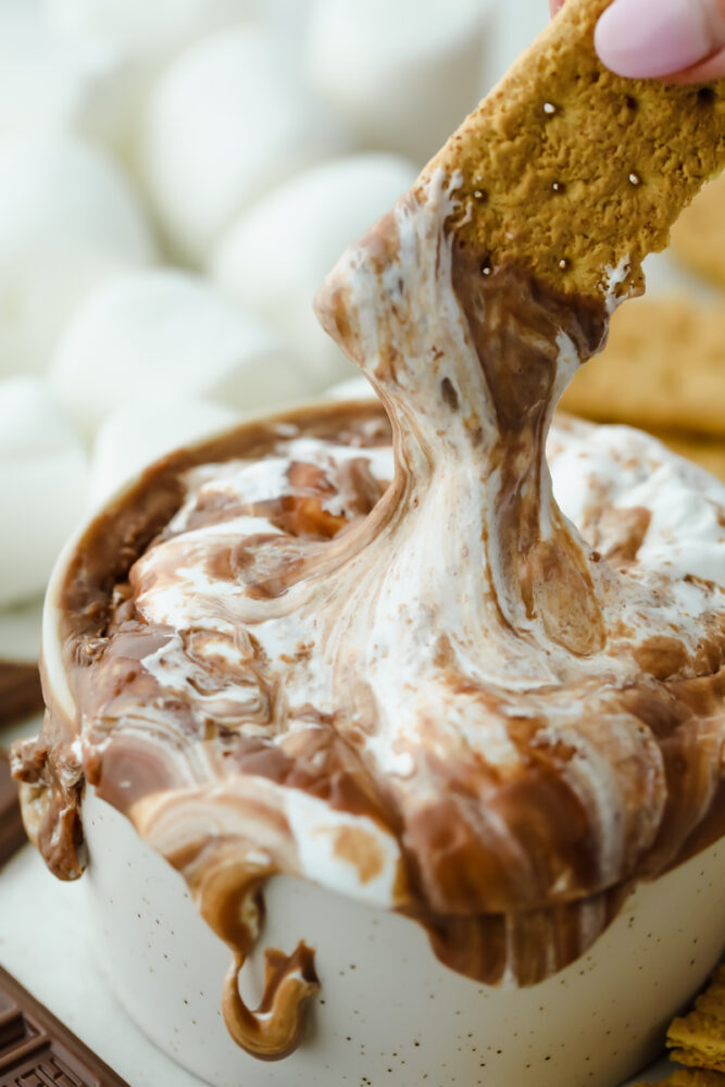 A graham cracker dipping into the chocolate and marshmallow. 