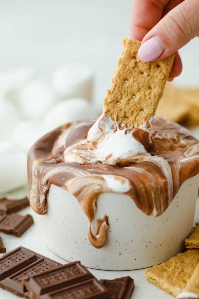 A graham cracker dipping into s'more dip. 