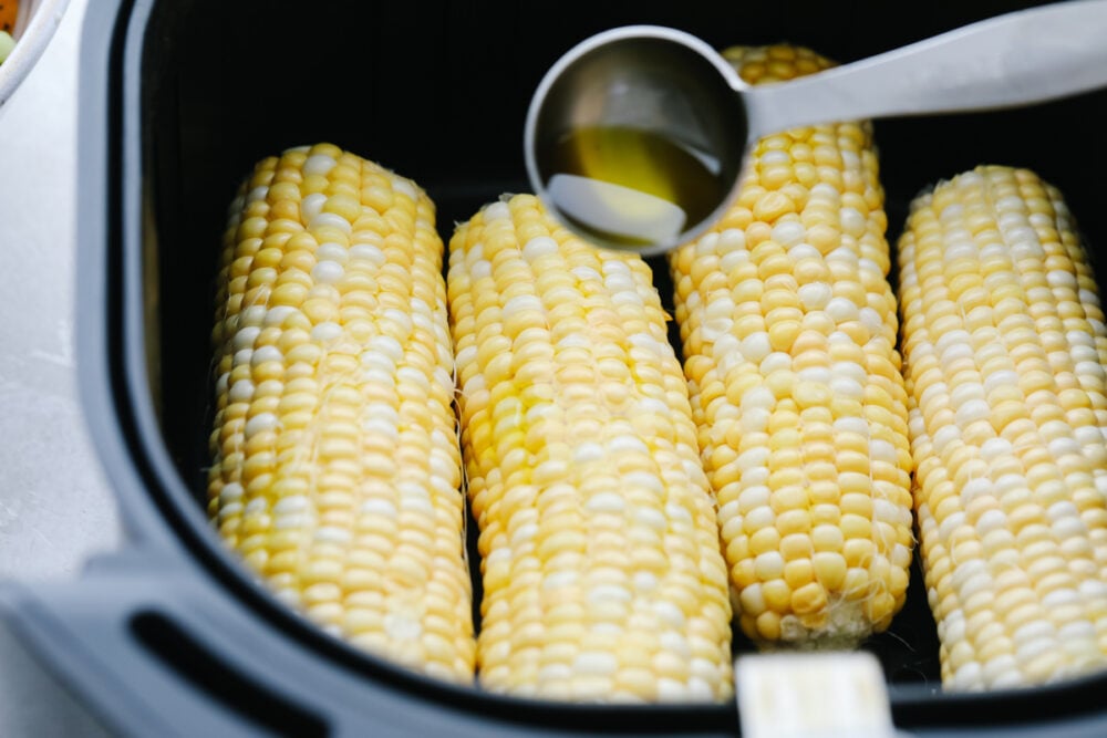 Drizzling the corn with olive oil before air frying. 