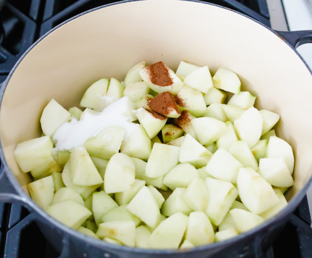 Chopped apples in a bowl with sugar and cinnamon being added as ingredients. 