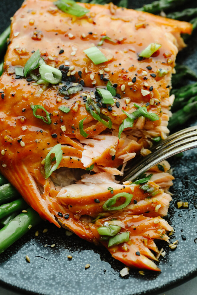 Taking a bite of asian glazed salmon, garnished with green onions.