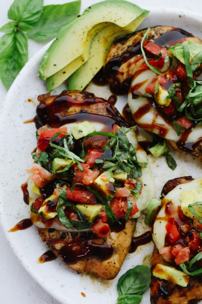 Grilled California Avocado chicken on a white plate with basil and sliced avocado garnish. 