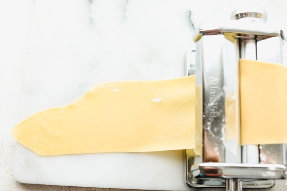 A long golden sheet of pasta getting thinner. 