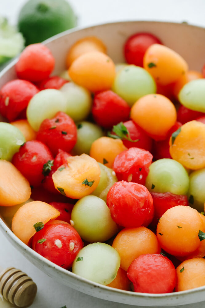 A bowl of fruit salad with melons and dressing. 