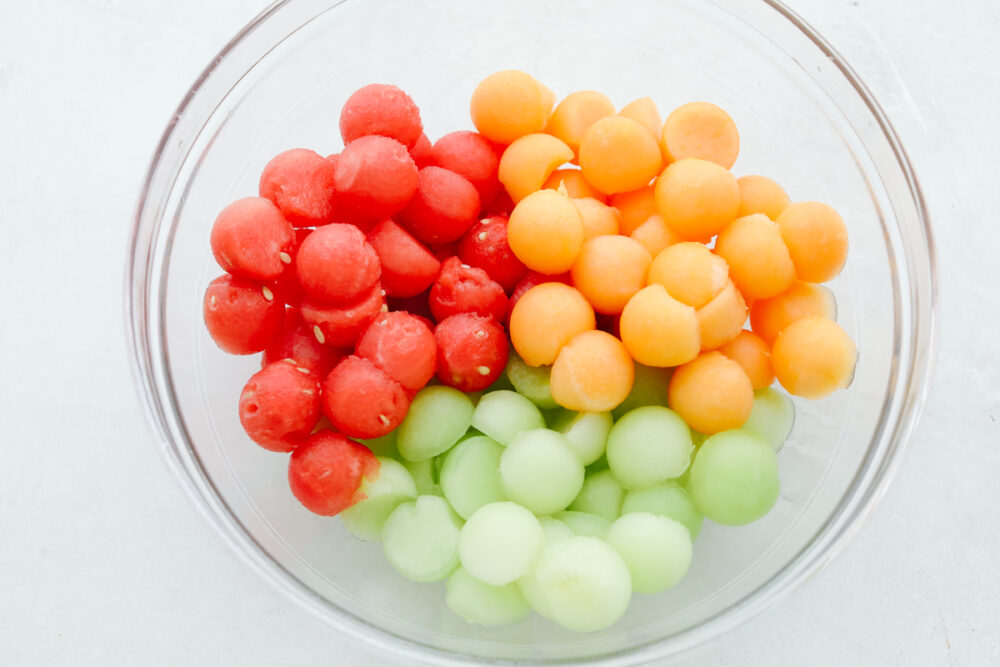 A bowl filled with fruit, all scooped as small pieces. 