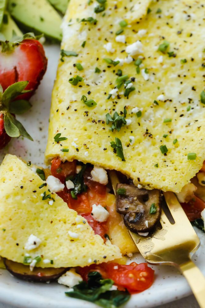 A fully cooked omelet on a plate with a fork cutting into it. 