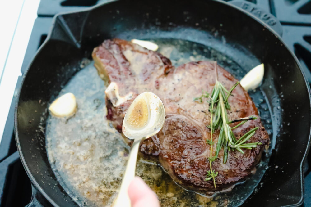 Spooning butter over ribeye steak. 