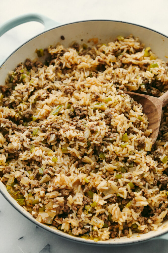 Rice with meat and veggies being served with a wooden spoon.