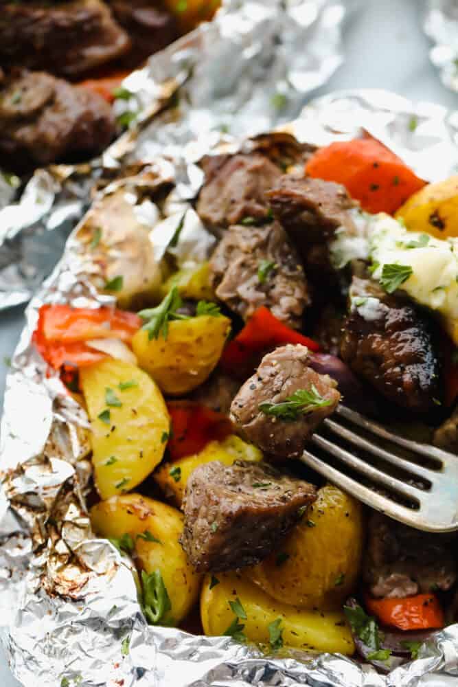 Steak foil packets opened with a fork in a steak. 