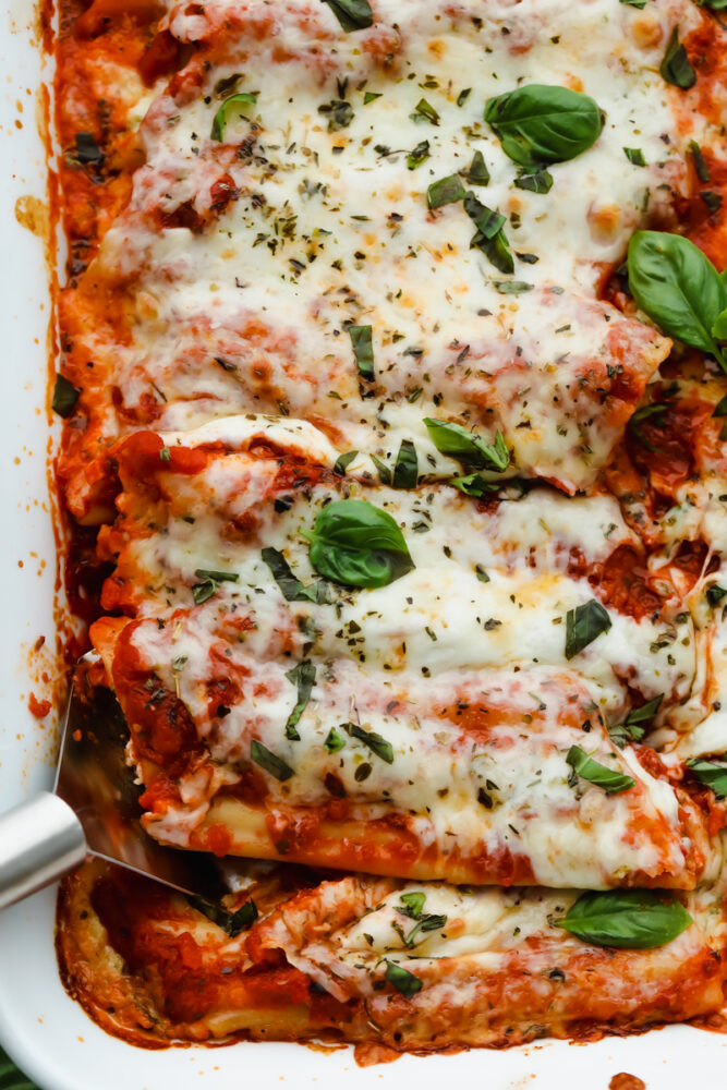 Manicotti being served with a serving spoon.