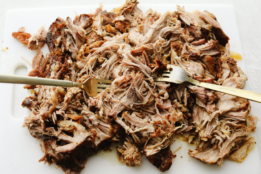 Pork being shredded with two forks. 