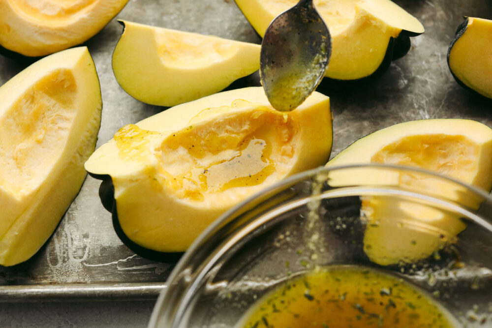 Oil and spices being drizzled on squash with a spoon. 