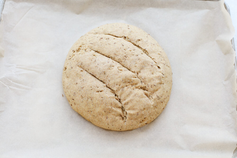 Formed round loaf of rye bread with cuts on a lined cookie sheet. 