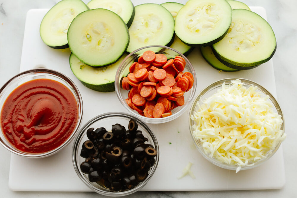 Zucchini pizza bite ingredients separated into small glass bowls.