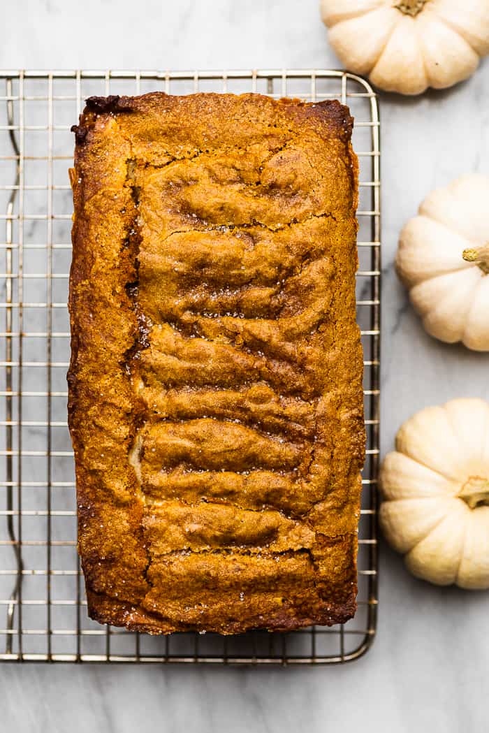 cream cheese pumpkin loaf on a cooling rack surrounded by white pumpkins.