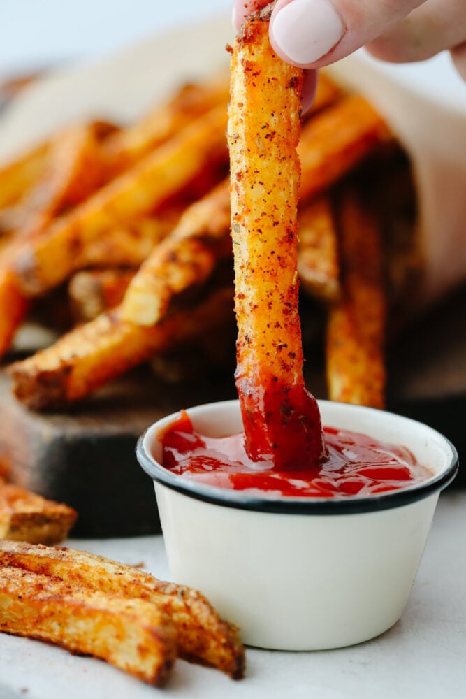 A cajun fry being dipped in ketchup. 