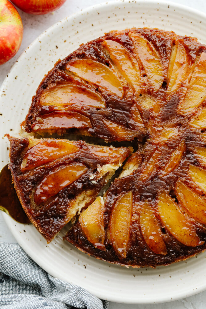 Taking a slice out of caramel apple upside down cake, served on a white dish.