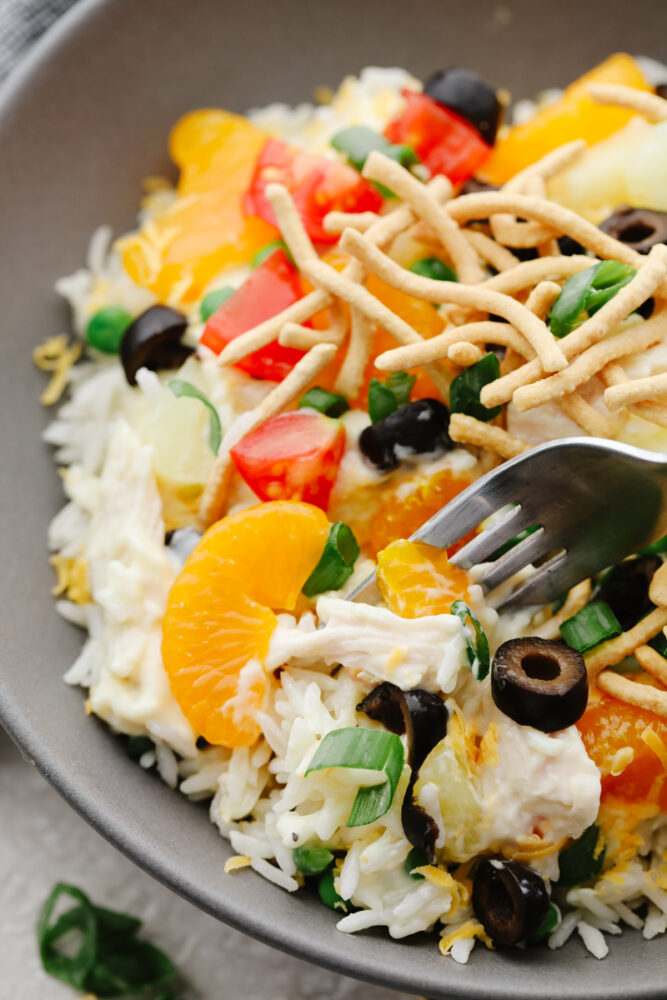 A closeup of a Hawaiian haystack with olives, mandarin oranges, tomatoes, and chow mein noodles as toppings.