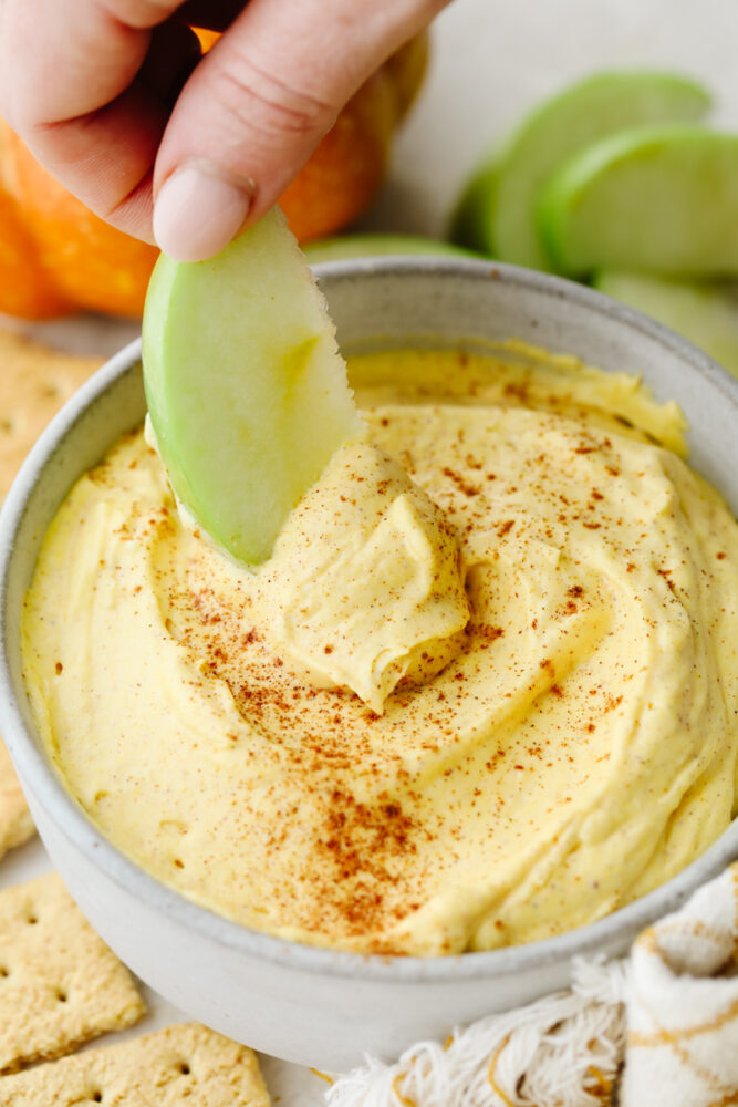 Someone dipping an apple into pumpkin pie dip. 