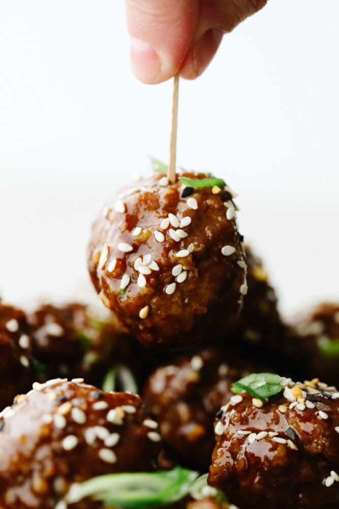 A toothpick being poked into a meatball. 