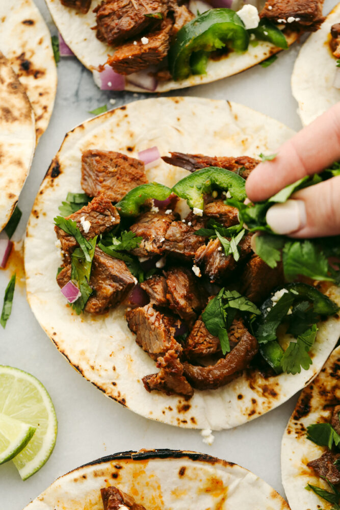 Beef brisket on a tortilla with someone putting on toppings. 