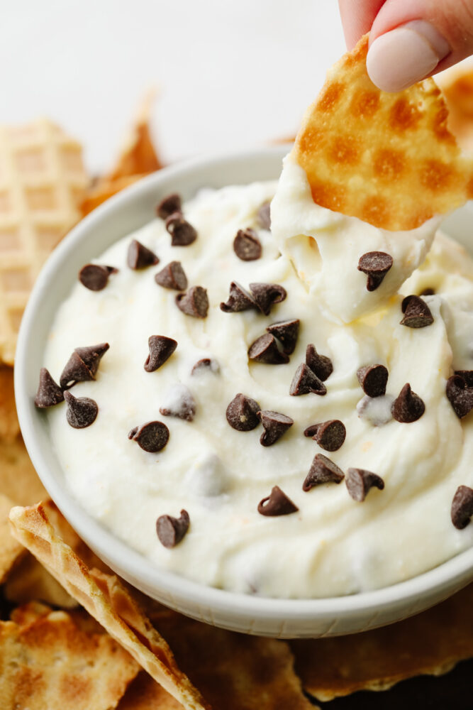 A piece of a waffle cone being dipped into the cannoli dip. 