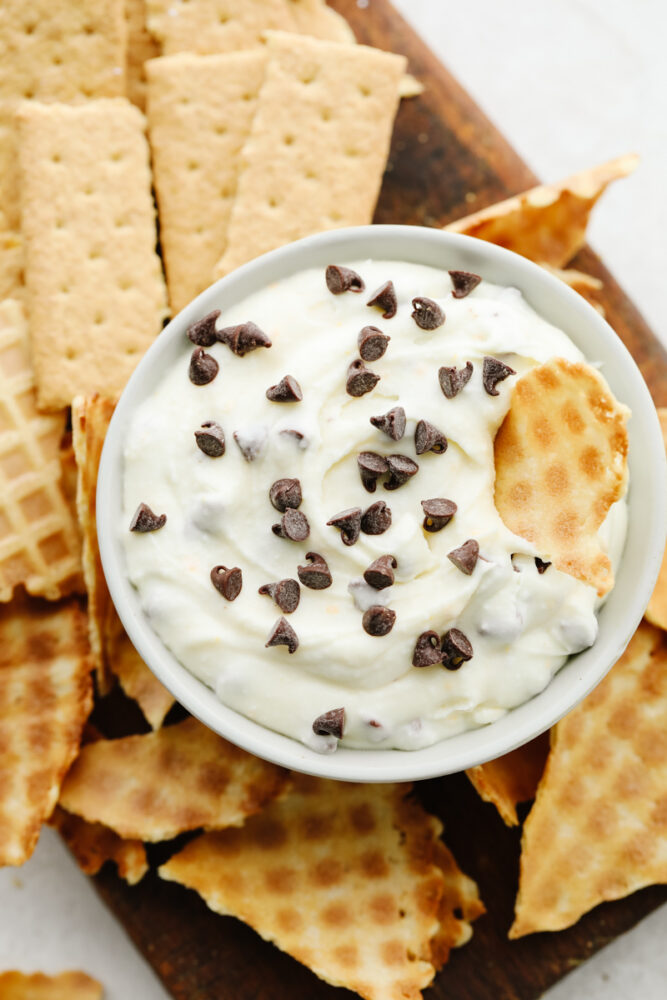 Cannoli dip with mini chocolate chips on a tray with broken up waffle cones and graham crackers. 