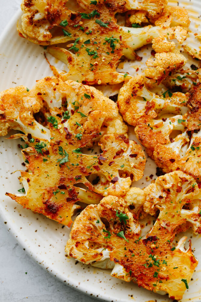 4 cauliflower steaks on a white plate.