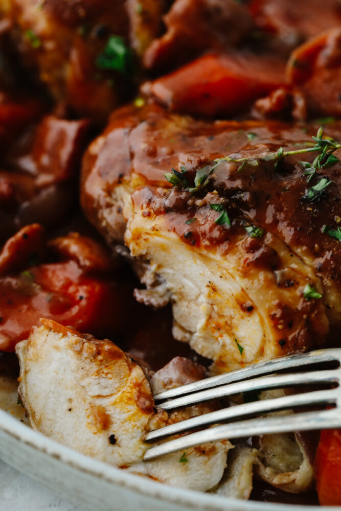 Coq au vin being cut into with a fork. 