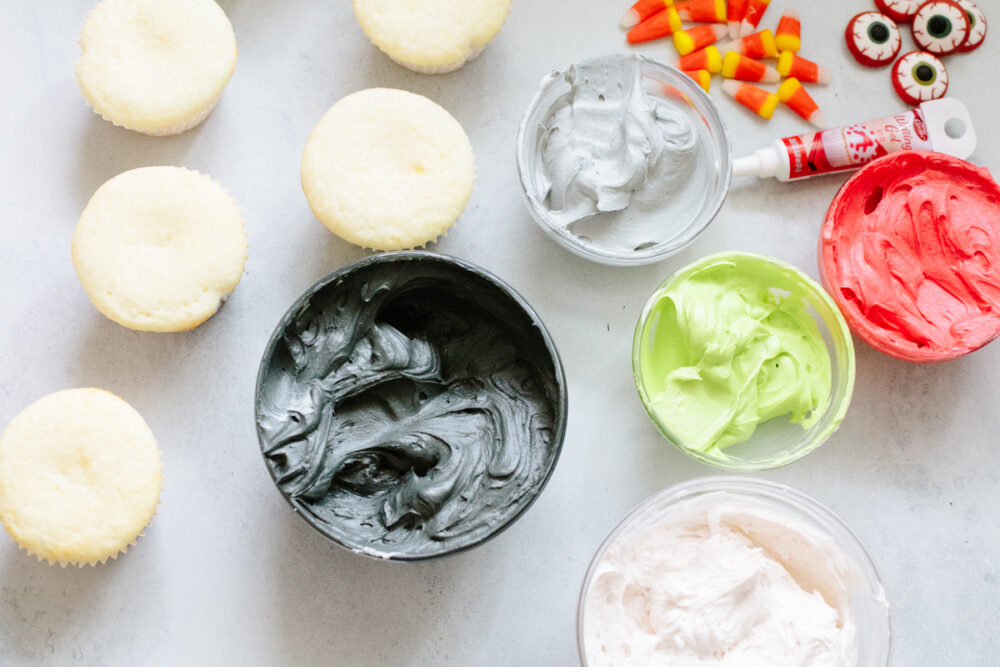 Various colors of frosting, decorations, and unfrosted cupcakes.