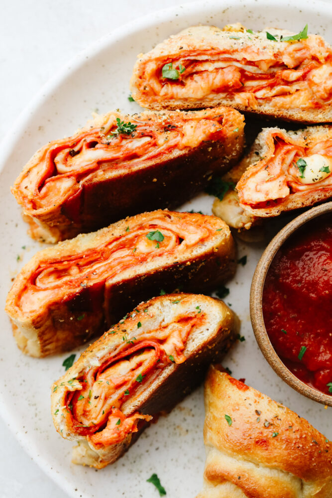 Slices of a pepperoni roll on a platter with some dipping sauce. 