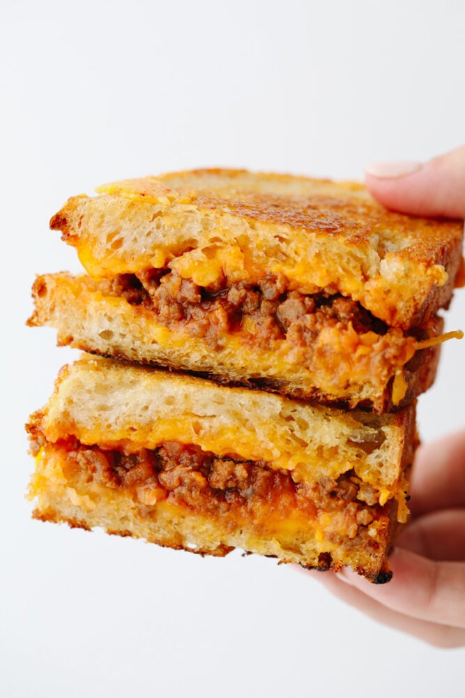 A hand holding 2 slices of a sloppy joe sandwich. 