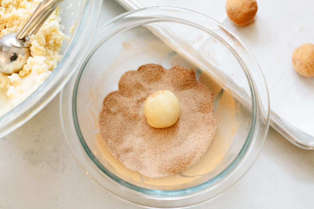 A snickerdoodle dough ball being rolled into cinnamon sugar. 