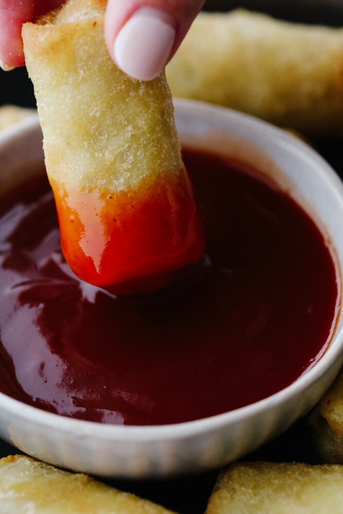 An egg roll being dipped into sweet and sour sauce. 