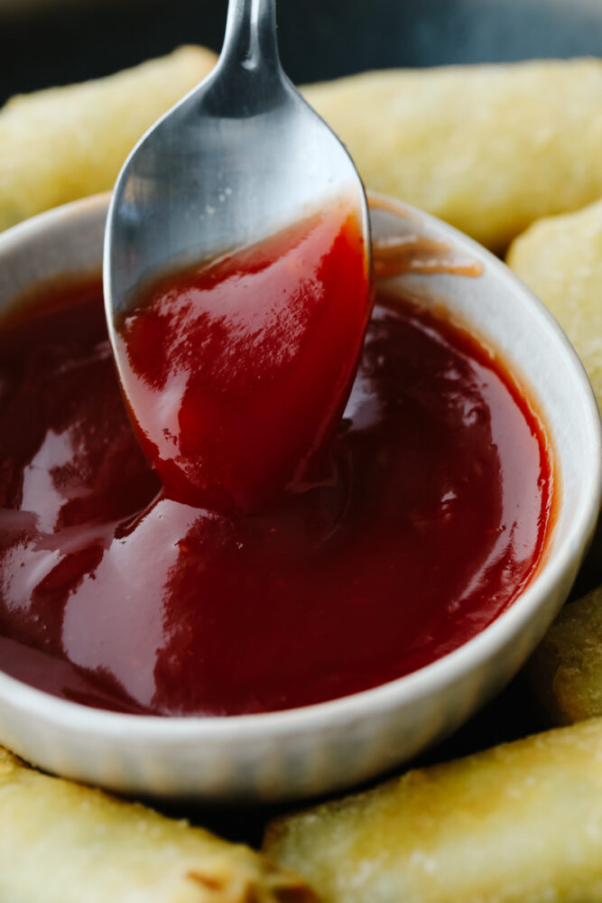 A spoon being dipped in sweet and sour sauce.