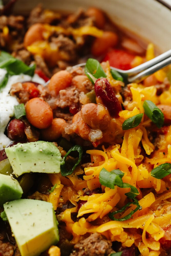 A close up of chili with a spoon scooping some out of a bowl. 