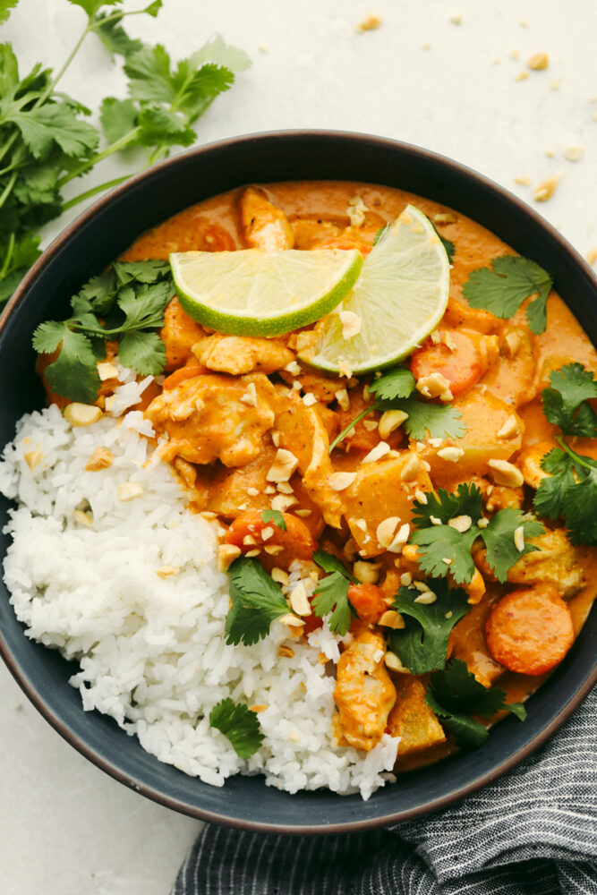 Massaman curry in a bowl with garnish and rice. 