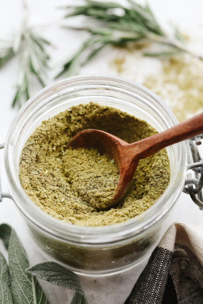 Getting a scoop of poultry seasoning out of a glass jar.