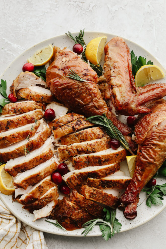 Sliced turkey on a white plate with rosemary, lemon, and cranberry garnish.