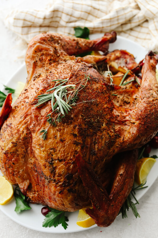 A full smoked turkey on a white plate with garnish.